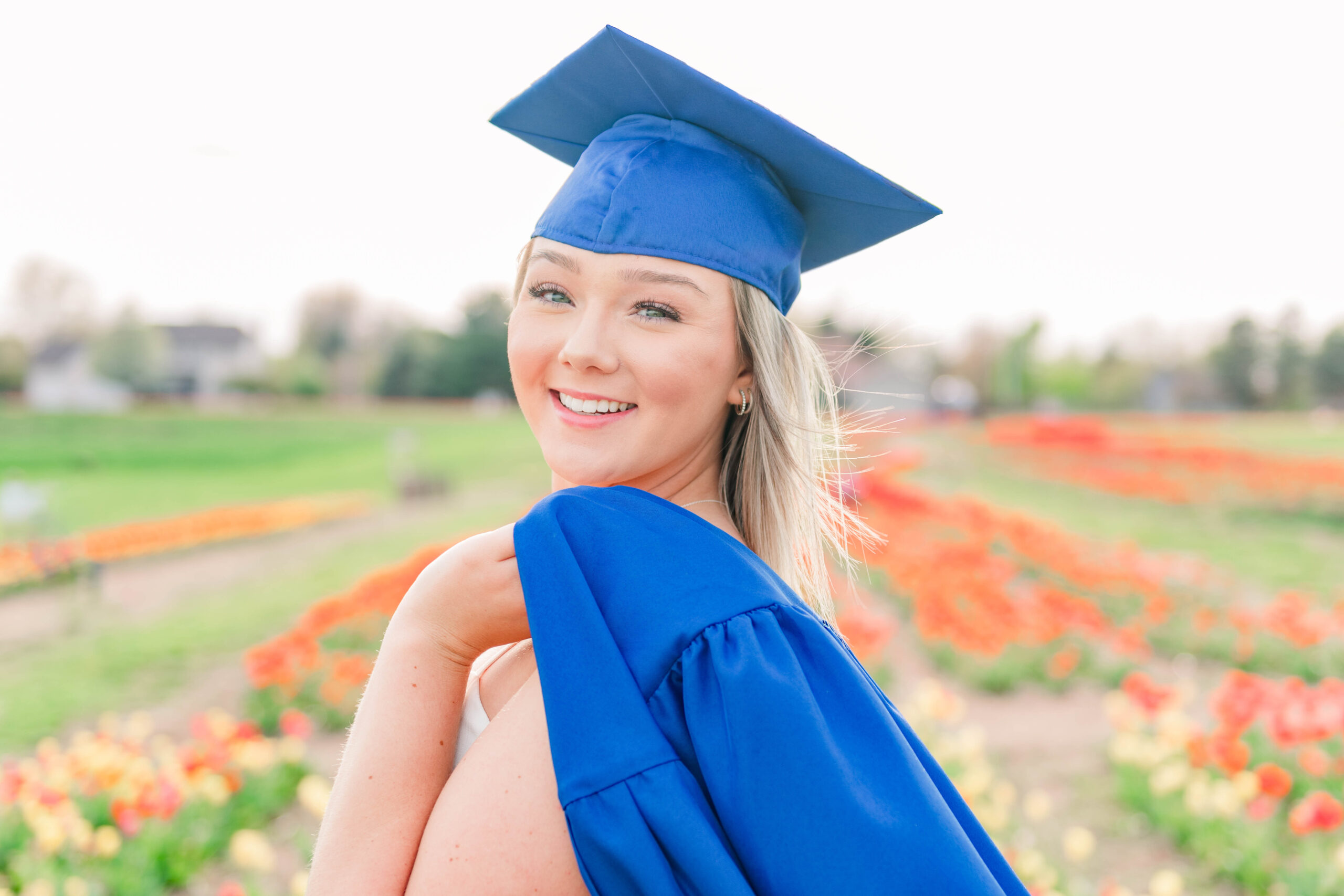 beautiful girl in tulip field in cap and gown for senior photo session