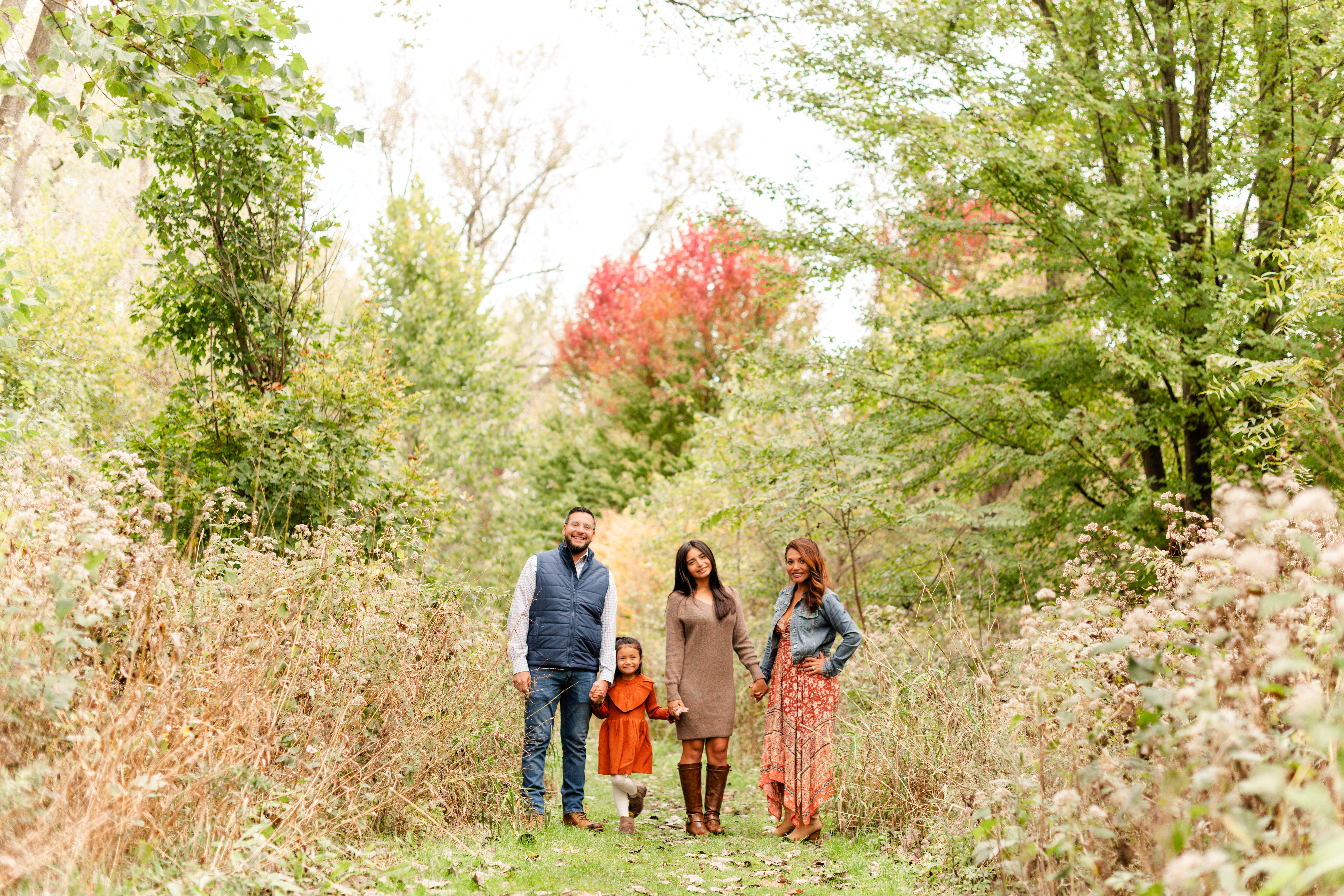 The Alvarez family holding hands surrounded by colorful fall leaves and trees in Lake Geneva, Wisconsin.