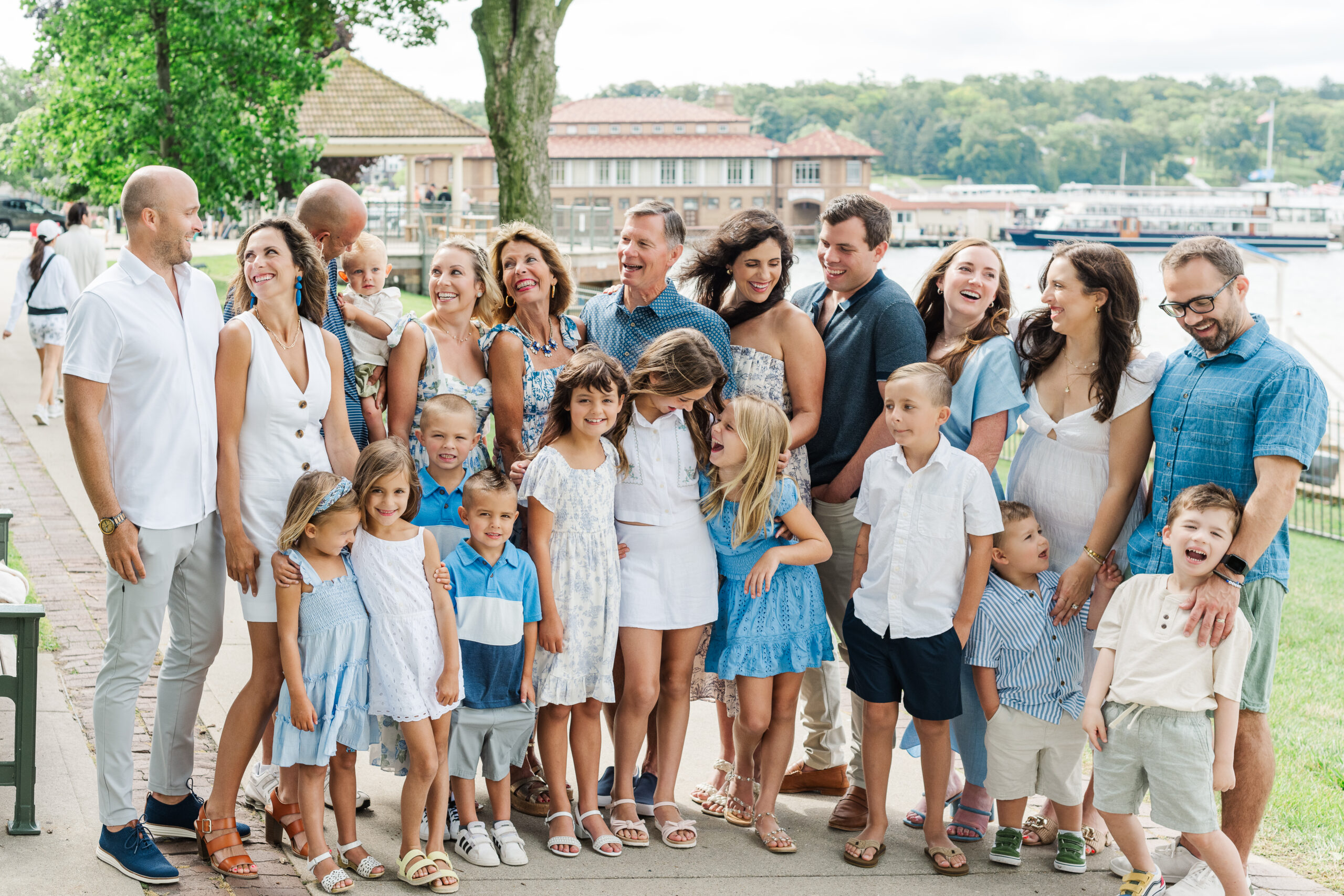 The Fairbanks family, a group of 22 in coordinated shades of blue, white, and cream, standing together in downtown Lake Geneva, Wisconsin, with the beautiful Riviera and lake as a backdrop.