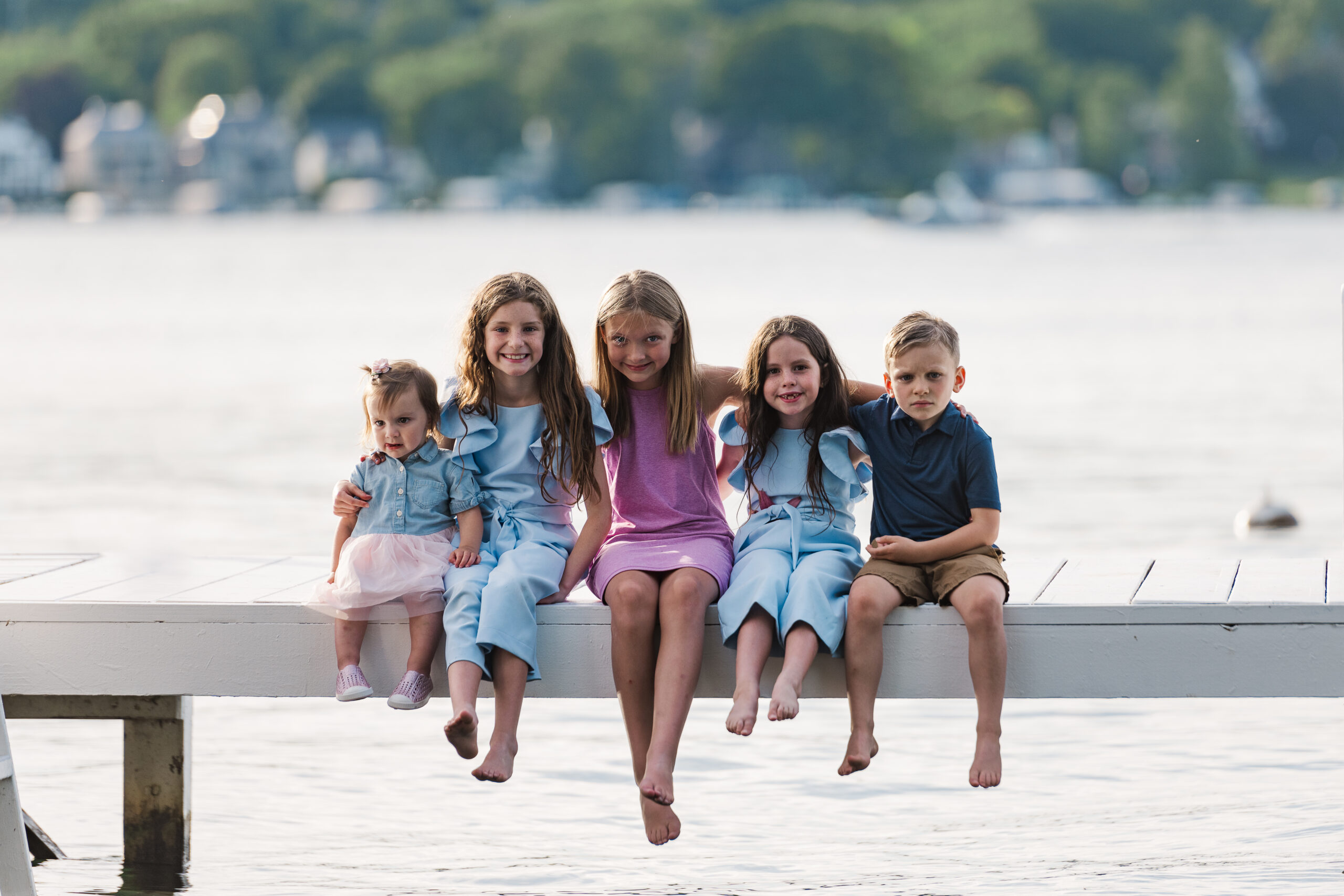 5 grandkids sitting on a dock with their feet dangling over the lake in the middle of summer