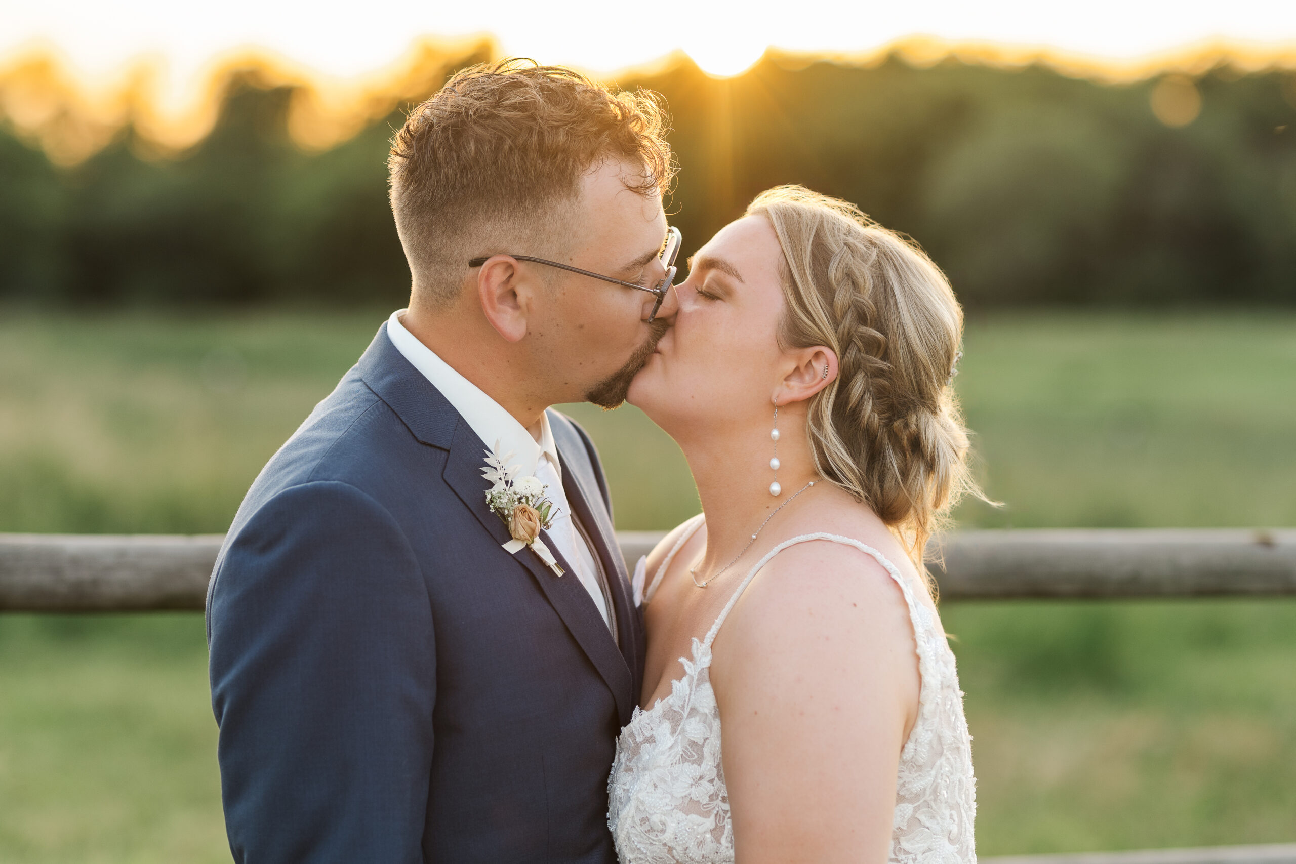 Bride and groom share a kiss at sunset with golden light glowing behind them at their outdoor wedding in Franksville, Wisconsin.